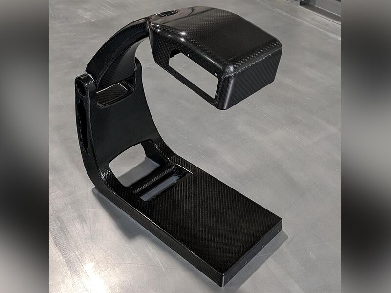 Image of the carbon fiber body of the portable X-ray machine, without sensors or paint. It is attached at a hinge and opened in its deployed state. The device is sitting on a steel table surface. The surface is carbon fiber weave with a high gloss finish.